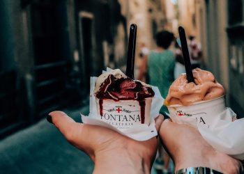 Crop anonymous couple with delicious ice cream in hands during walk in narrow street in historic city centre