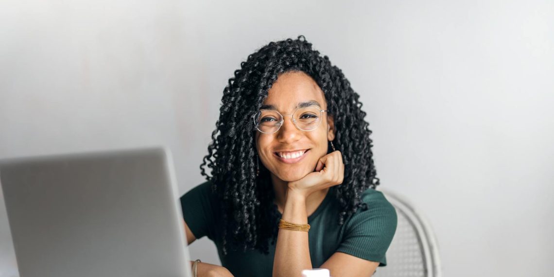Happy ethnic woman sitting at table with laptop